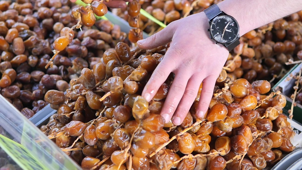 Man's Hand Picking Fresh Dates from a Market Display