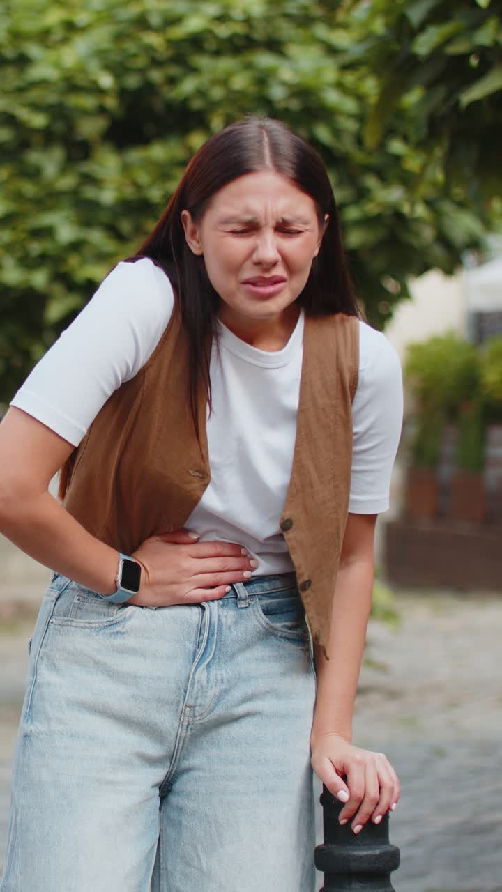 Caucasian young woman traveler feeling sudden strong abdominal stomach pain problem on city street
