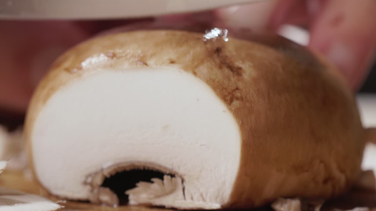 primer plano de las manos mientras cortan setas en una tabla de cocina de madera