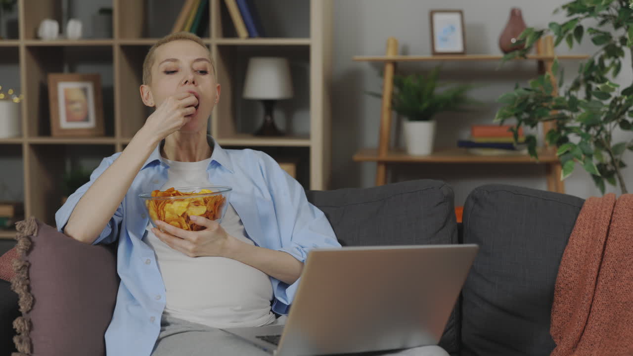 Pregnant Woman Eating Chips and Working on Laptop