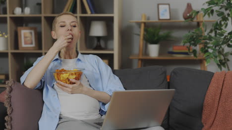 pregnant woman eating chips and working on laptop