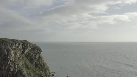 Aerial-flyover-of-drone-pilot-on-top-of-sea-cliffs,-calm-ocean-beyond