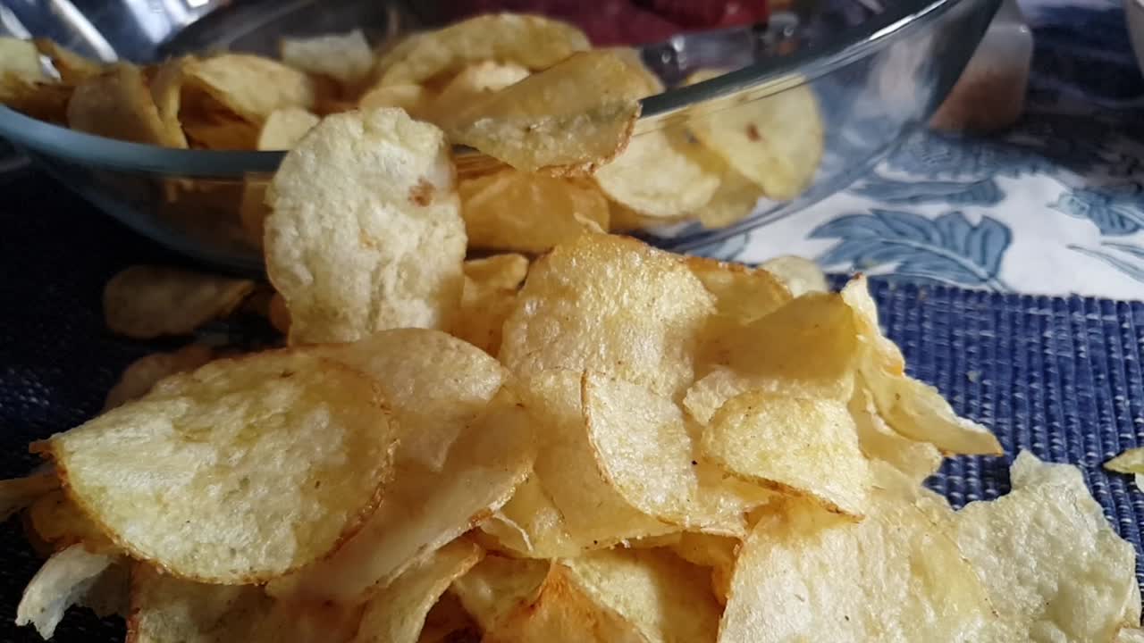 Crispy thin sliced kettle fried salted Potato chips falling down in slow motion on dinner table cloth, balsamic vinegar snack