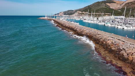 Port-ginesta-marina-with-moored-sailboats,-clear-blue-waters-on-a-sunny-day,-barcelona,-spain,-aerial-view