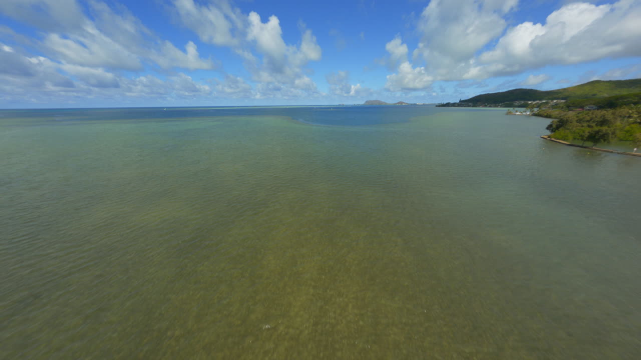 volando sobre la bahía de kaneohe, fpv drone sobre la costa este de oahu de kaneohe, kailua, en un día soleado de verano con nubes esponjosas arriba y botes en el agua