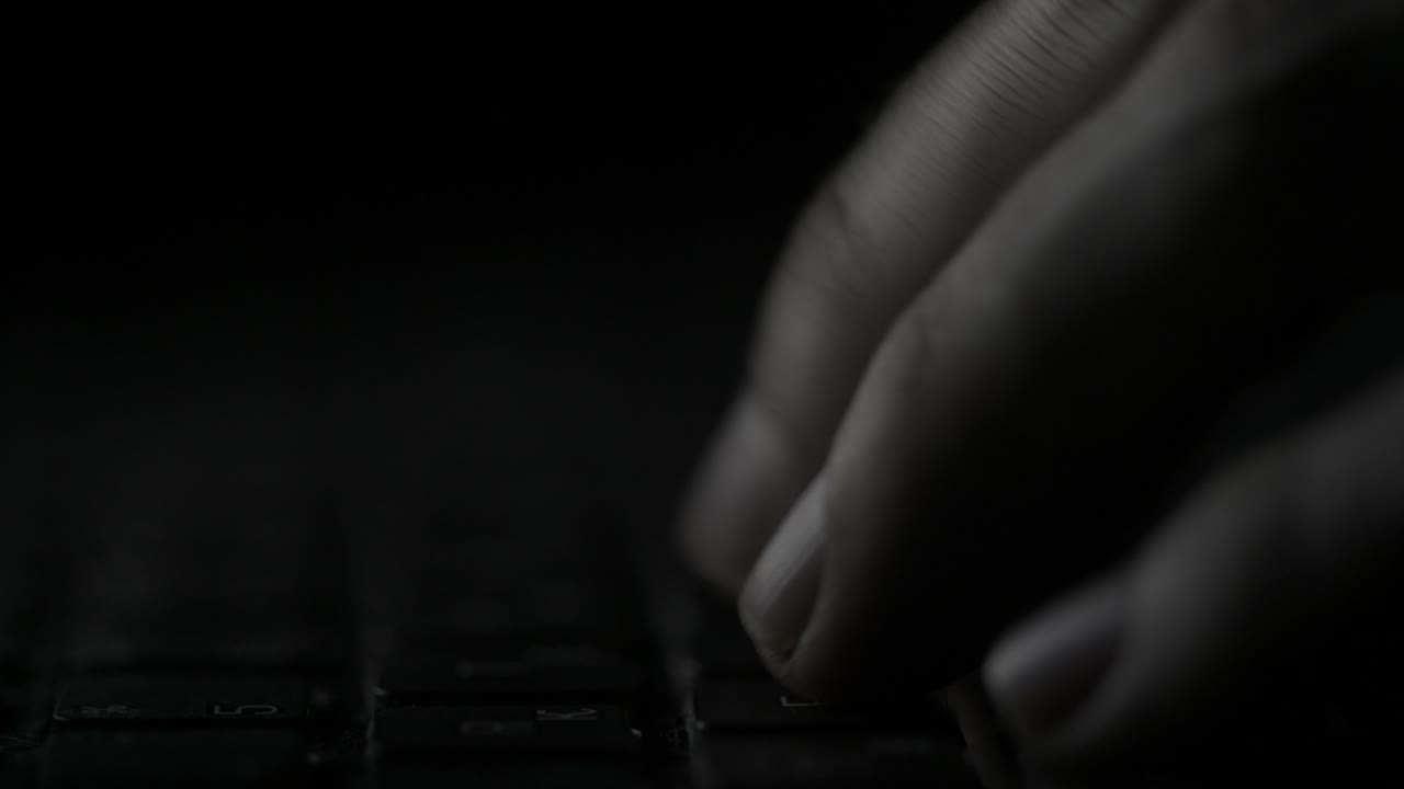 manos escribiendo en un teclado de portátil con poca luz