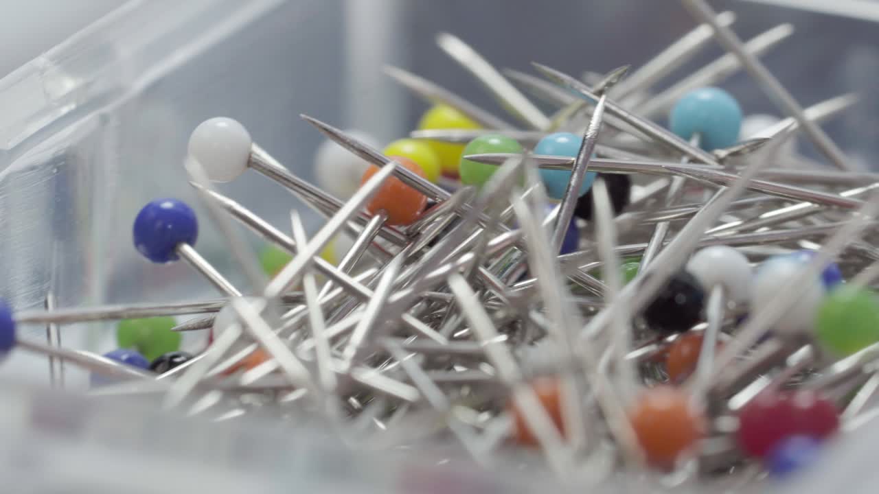 Close up of colored sewing pins with metallic heads inside a transparent plastic container, macro shot