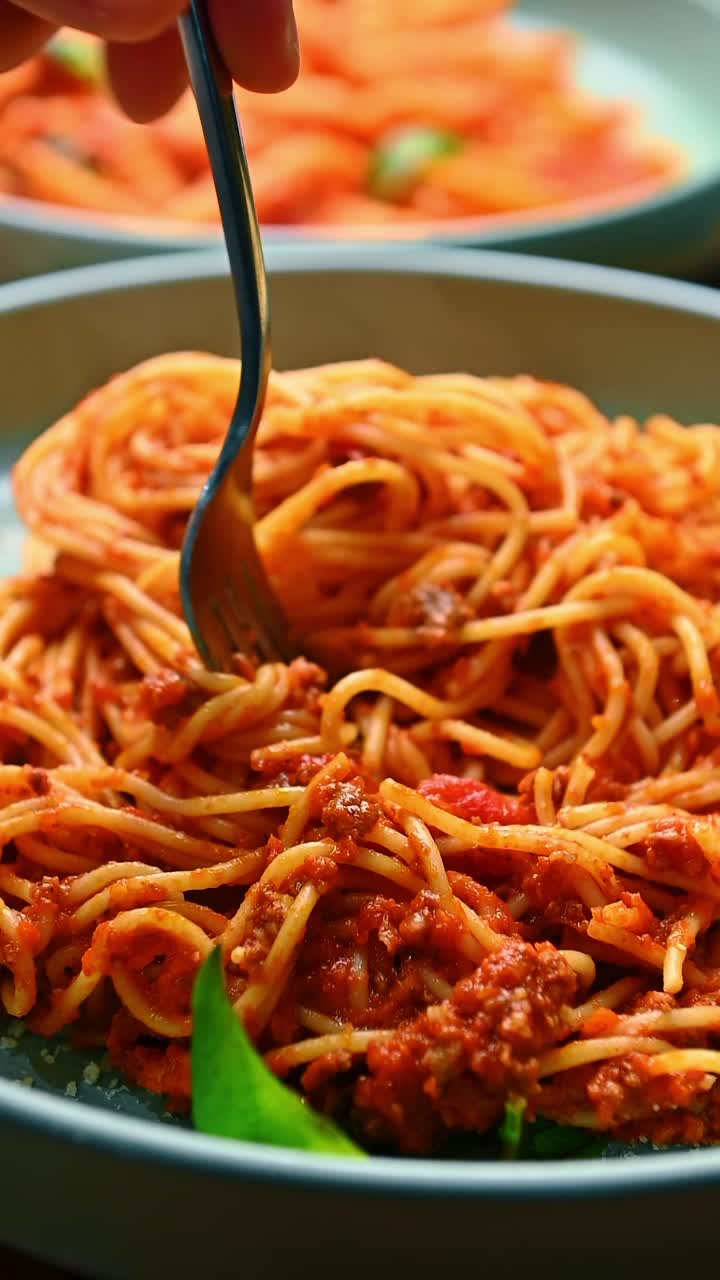 Spaghetti sollevati dalla forchetta, guarniti con salsa di pomodoro. Vista macro della pasta sollevata da una forchetta metallica su un piatto con sfondo sfocato.