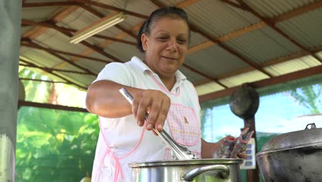 handheld tracking shot: a lady, wearing an apron, cooking something in a big pot