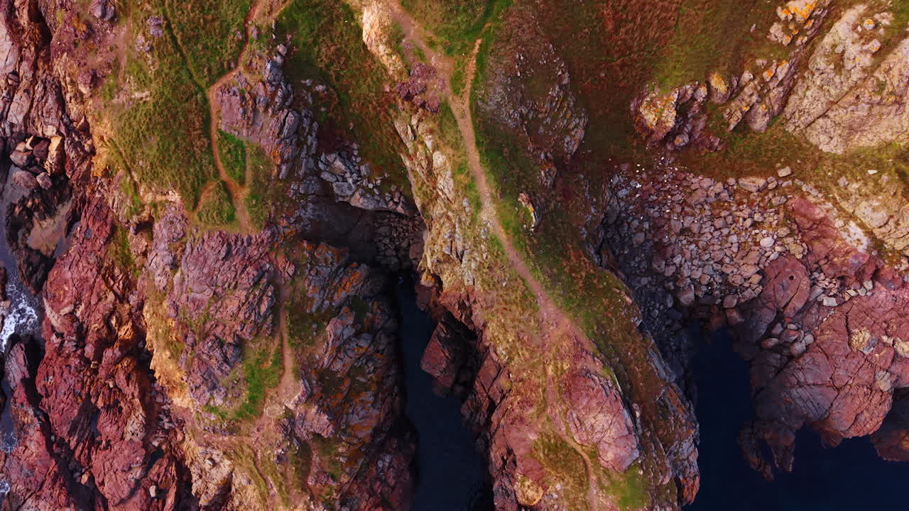 Vista aerea di scogliere rocciose con sentiero e mare. Ripresa aerea di spettacolari scogliere rocciose lungo la costa. Formazioni rocciose rosse e marroni con chiazze di verde e uno stretto sentiero costiero