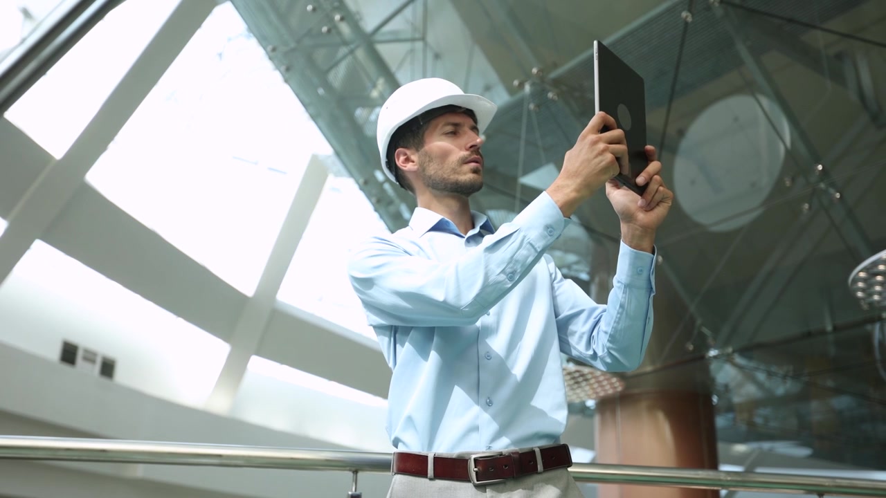 Professional Engineer in Hard Hat Inspecting Modern Building with Tablet