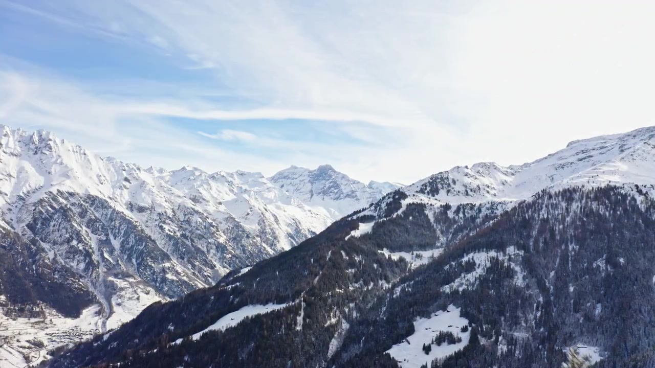 Volo attraverso una fitta foresta alpina innevata che si apre su un panorama montano mozzafiato nelle Alpi svizzere durante l'inverno.