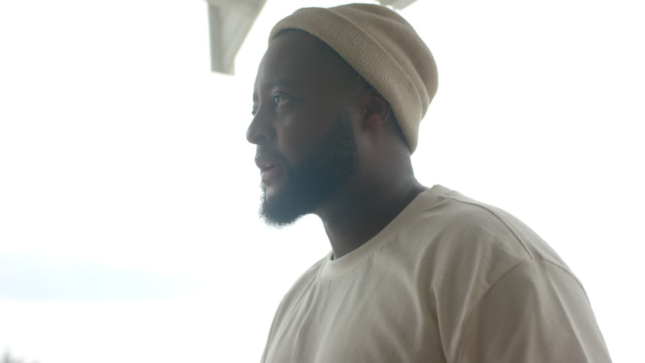 Homme afro-américain consultant une tablette sur le porche, marquant une pause et se retournant, regardant au loin, se frottant le menton.