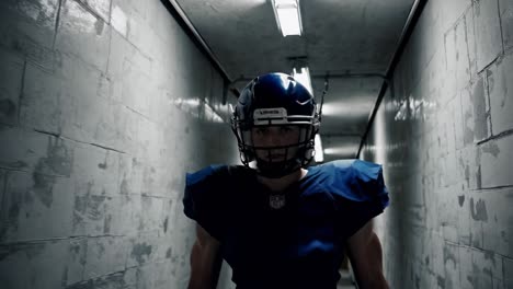 young, confident american football player wearing a helmet and pads, walking down a concrete corridor toward the field, exuding determination and readiness for the upcoming game