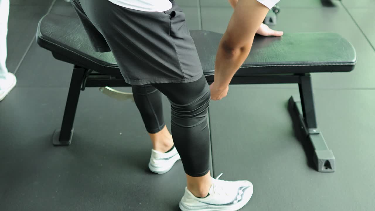 Athletic man adjusts flat workout bench in modern, well-lit gym, preparing for exercise