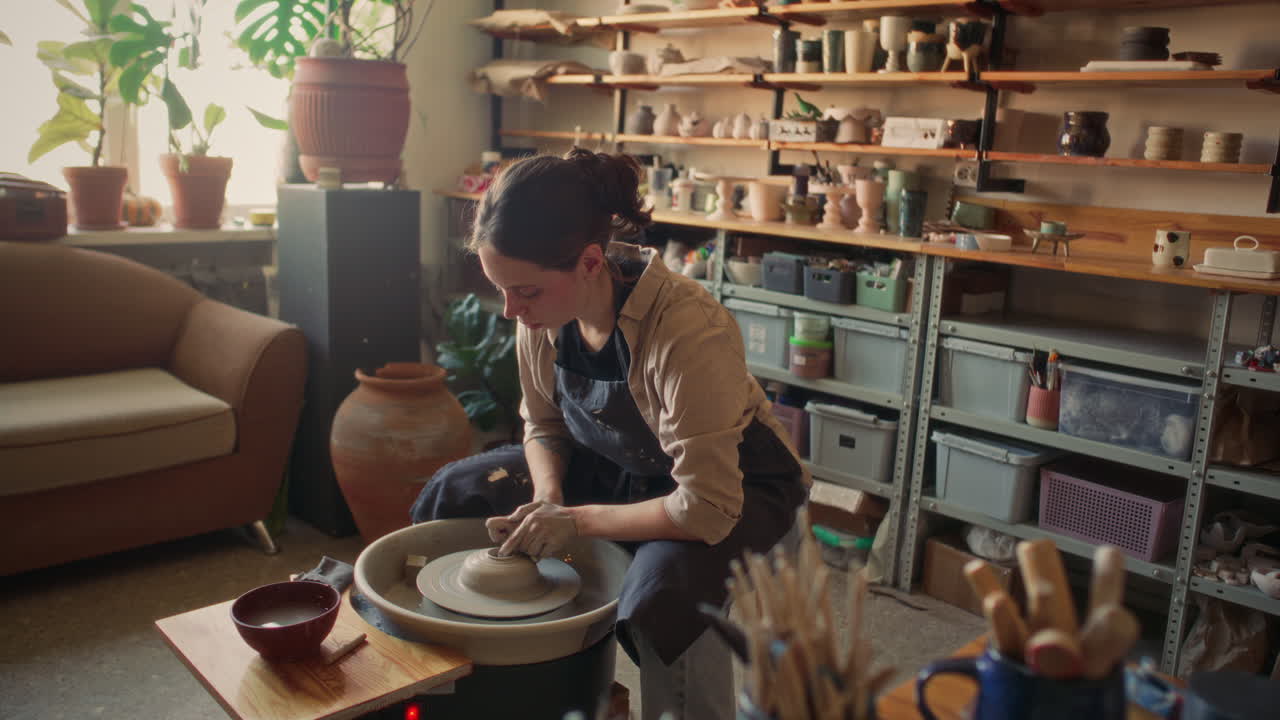 Young Woman Shaping Clay on Pottery Wheel in Cozy Ceramic Workshop