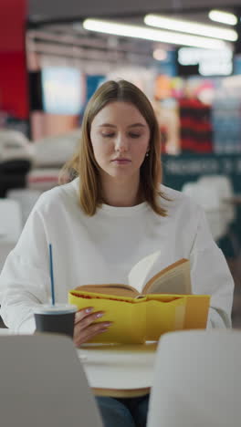 dama blanca sentada en un centro comercial leyendo un libro con una taza de café y una bolsa de compras cerca, la iluminación suave crea una atmósfera relajada con un fondo borroso