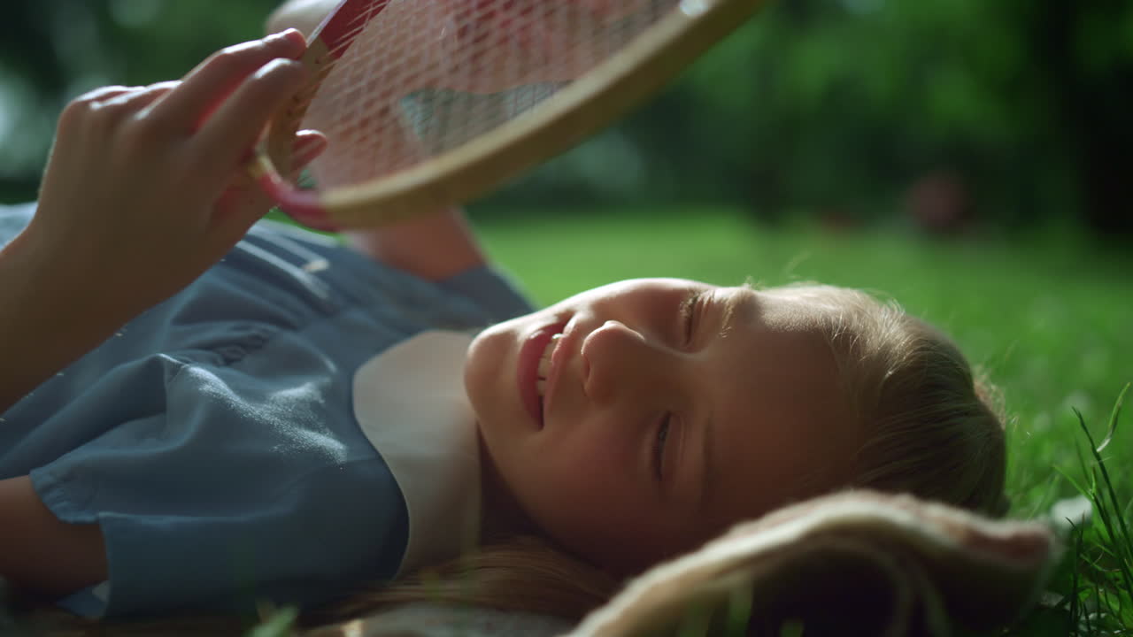 Dreamy girl lying on blanket touching racket strings in golden sunlight closeup