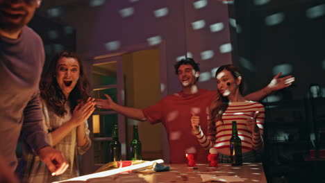 party friends playing beer pong at home disco lights. happy man tossing ball