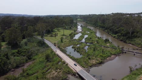 Drohne-Fliegt-über-Eine-Autobahnbrücke-über-Einen-Braunen-Fluss,-Eine-Pipeline-Ist-Ebenfalls-Sichtbar