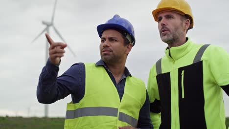 Ingenieros-Varones-Caucásicos-Y-Latinos-Parados-En-El-Campo-De-Turbinas-Eólicas-Y-Discutiendo-Juntos.