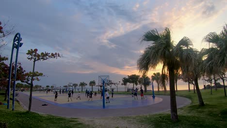 teenagers play pick up games of basketball at ocean side courts with evening sunset in background.