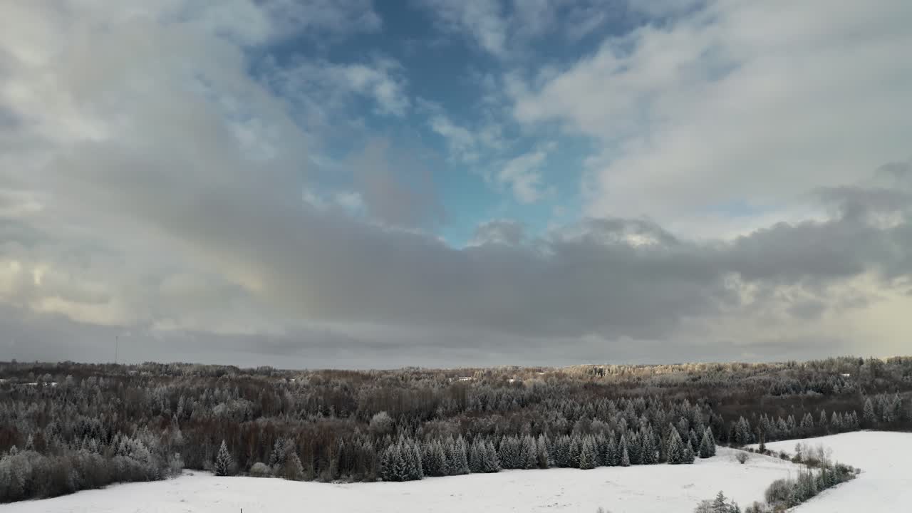 Flying over countryside landscape in snow covered winter season. Aerial drone view of beautiful sky over the forest. Frozen forest trees in bright winter day. Clean environment.