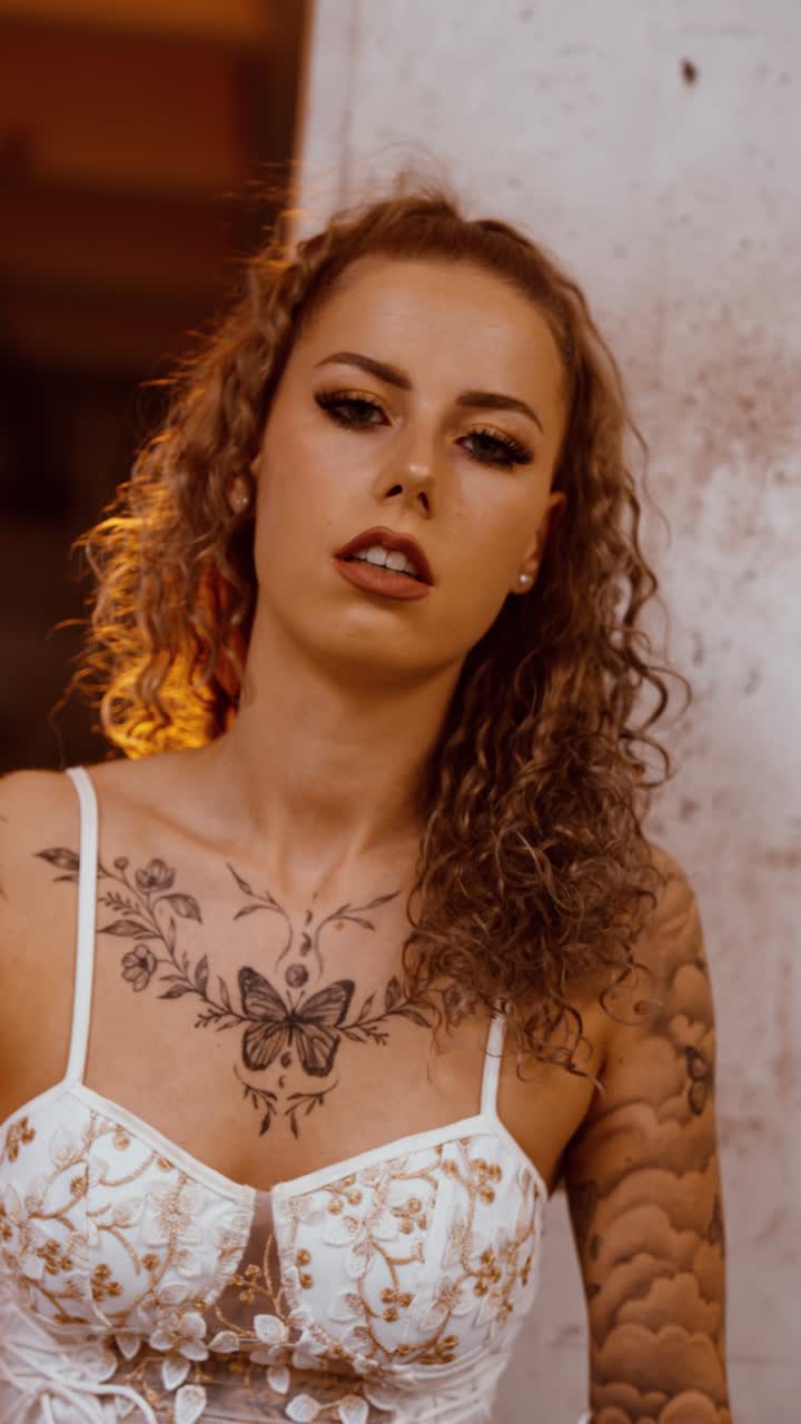 Vertical video of tattooed woman posing at warehouse pillar as fire ignites behind close up