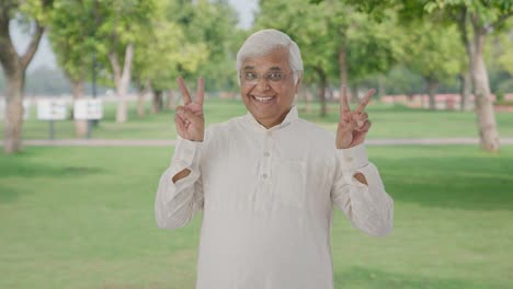 Happy-Indian-old-man-showing-victory-sign-in-park