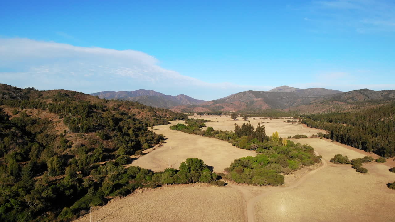 Aerial view of a landscape with field, mountains, trees, sky, and clouds
