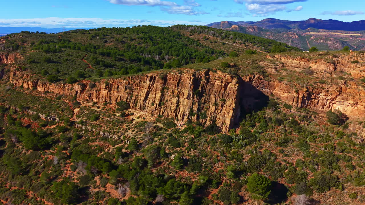 Paesaggio roccioso con alte scogliere e alberi verdi sotto un cielo blu nuvoloso, in un ambiente naturale di giorno.