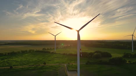 Große-Windkraftanlagen-Mit-Rotorblättern-Im-Feld,-Luftaufnahme,-Leuchtend-Orangefarbener-Sonnenuntergang,-Blauer-Himmel,-Windpark,-Zeitlupe,-Drohnendrehung