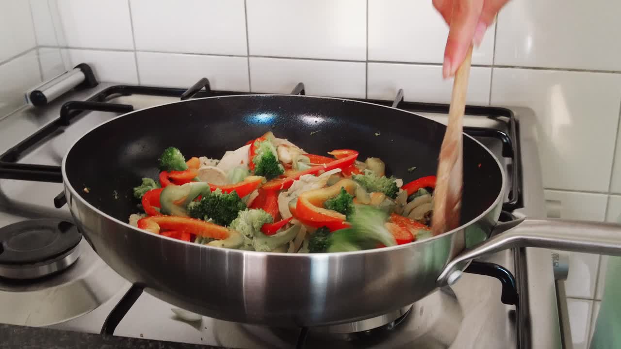 mujer revuelve una cuchara de madera a través de verduras en una sartén casera fogata saludable