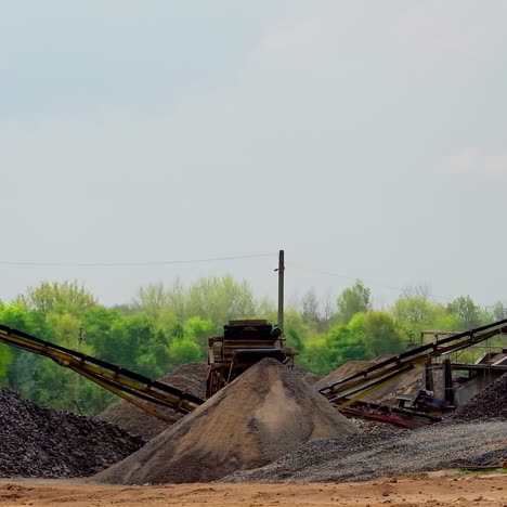 construction works. piles of stones on the ground and industrial machine on green nature background. heaps of crushed rocks in sunny day.