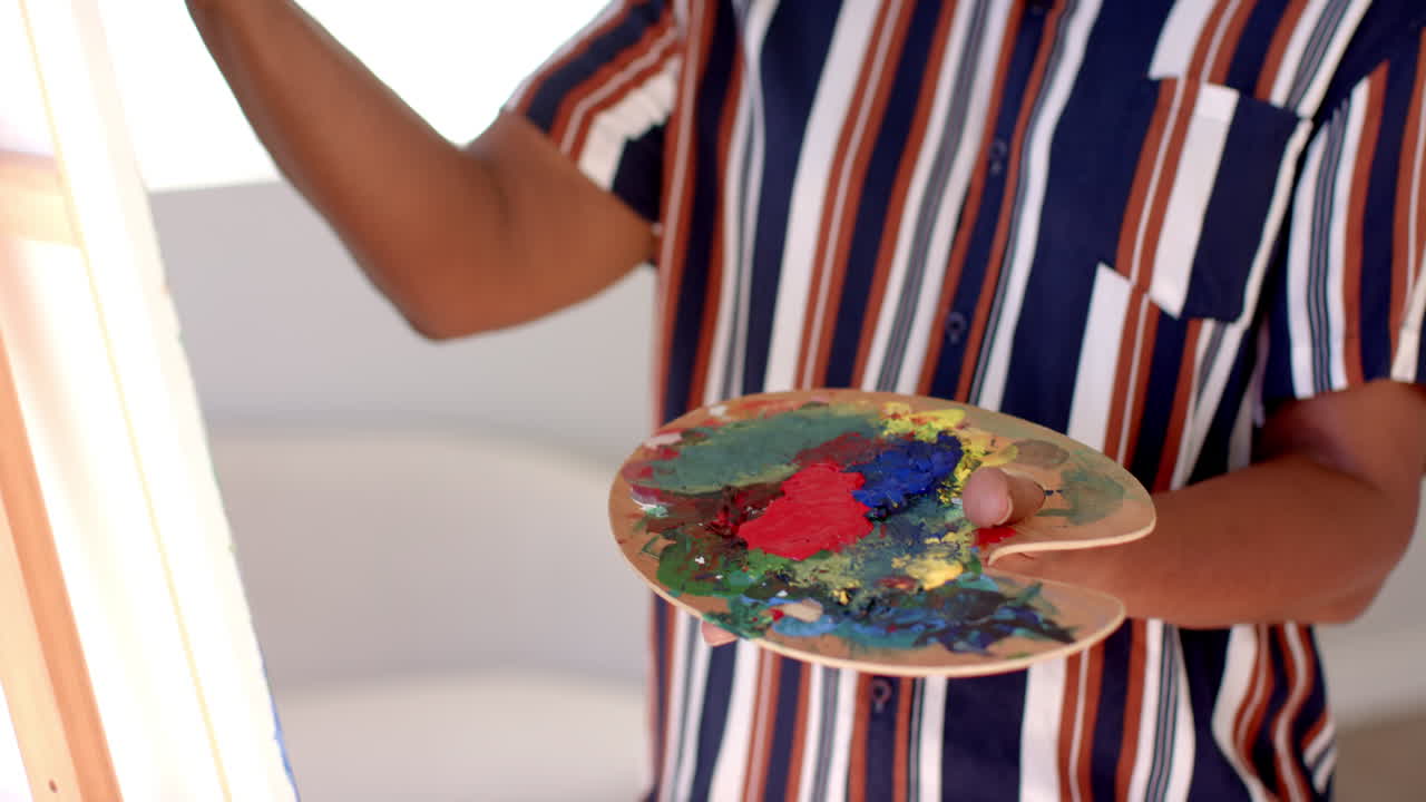 A senior African American woman is painting, holding colorful palette