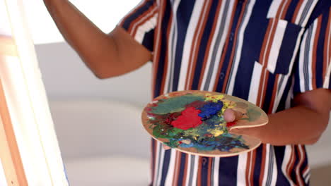 a senior african american woman is painting, holding colorful palette