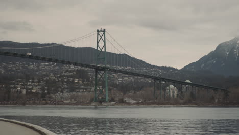 wide panning shot of lions gate bridge and snow packed mountains on cloudy morning