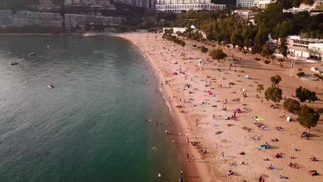 A-moving-aerial-view-of-visitors-at-Repulse-Bay-beach-in-Hong-Kong-as-public-beaches-reopening,-after-months-of-closure-amid-coronavirus-outbreak,-to-the-public