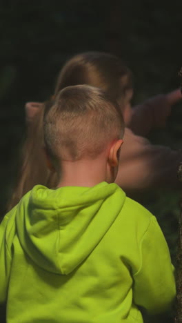 children walk in night nature park together. brother with elder sister explore woods at nighttime. active little kids adventure on vacation