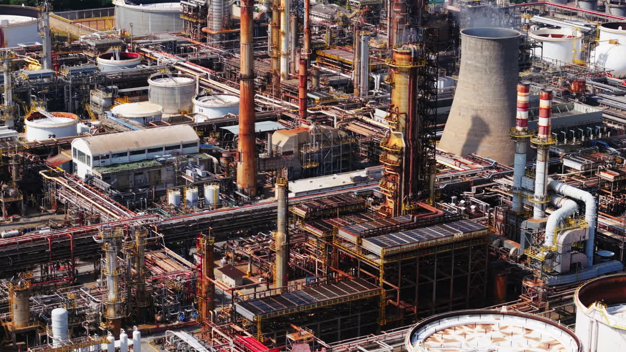 Drone panning shot over a dense oil refinery in Sicily, showing tanks, chimneys, and metal structures