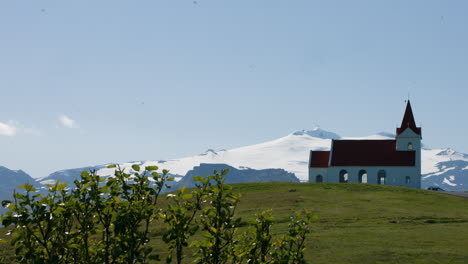 stone church ingjaldsholskirkja on green hill, snæfellsjökull glacier behind