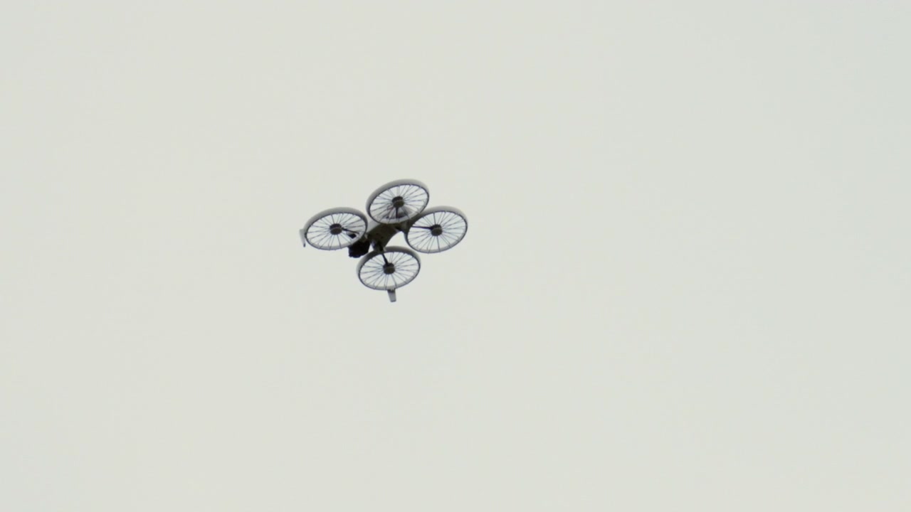 A drone flying high in a clear sky, captured from below with a minimalistic background