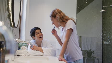 Feliz-Pareja-De-Lesbianas-Caucásicas-Cepillándose-Los-Dientes-Juntas-Y-Sonriendo-En-Un-Baño-Soleado