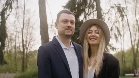 retrato de una pareja elegante sonriendo a la cámara y luego mirándose mientras están en el parque