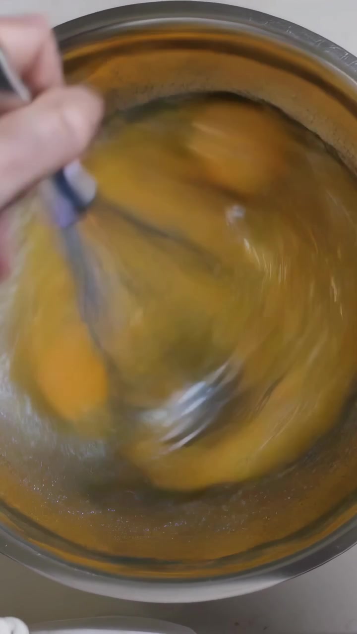 Video verticale: Sollevando la frusta, mano che sbatte due uova in una ciotola d'acciaio sul bancone della cucina per cucinare