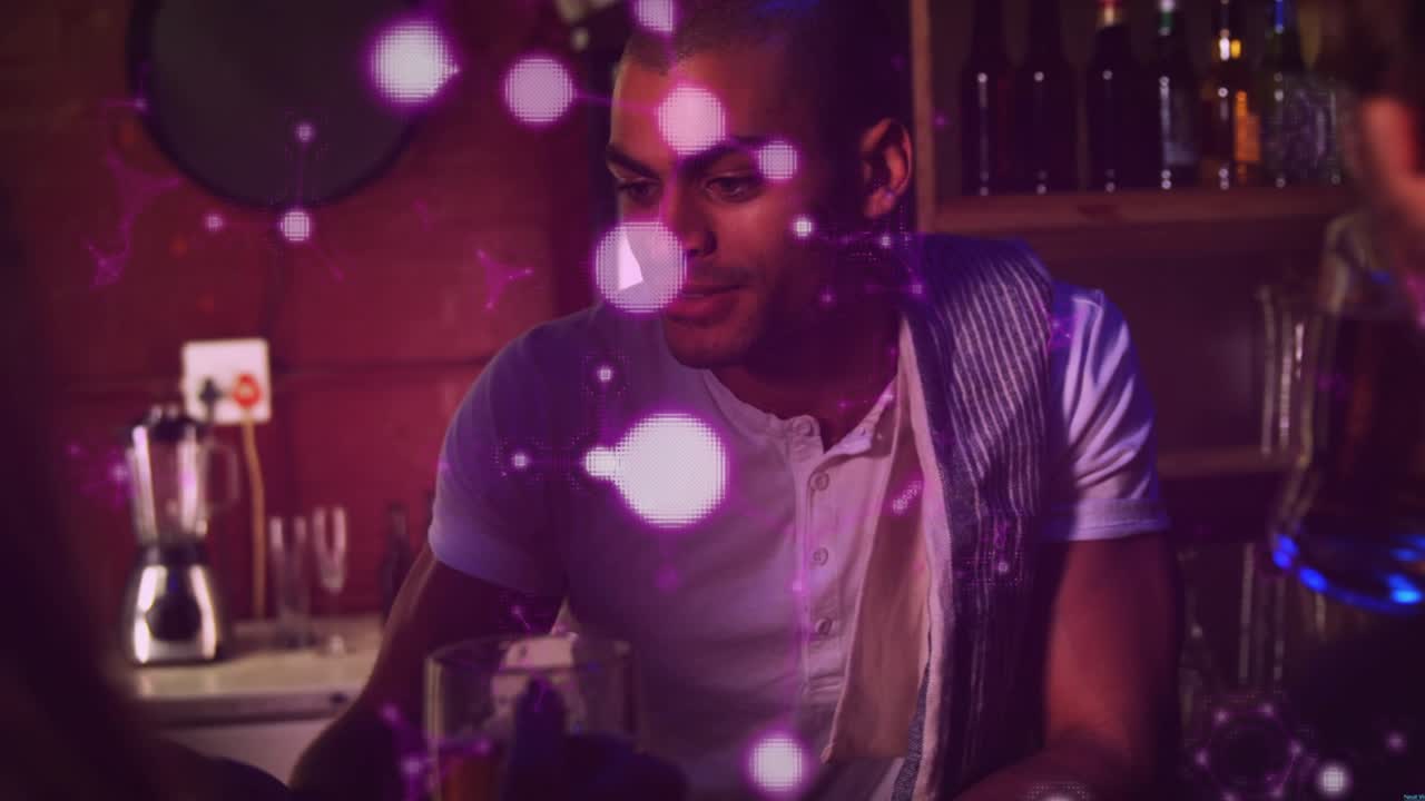 Man leaning at bar responding to conversation and reaching for glass while purple bokeh overlaying