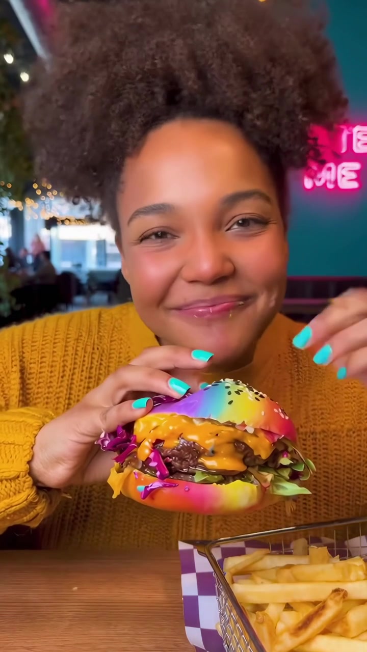 Happy Woman Takes a Big Bite of a Vibrant Rainbow Burger