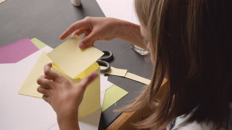 top view of blonde girl cutting cardboard and building geometric shape sitting at desk