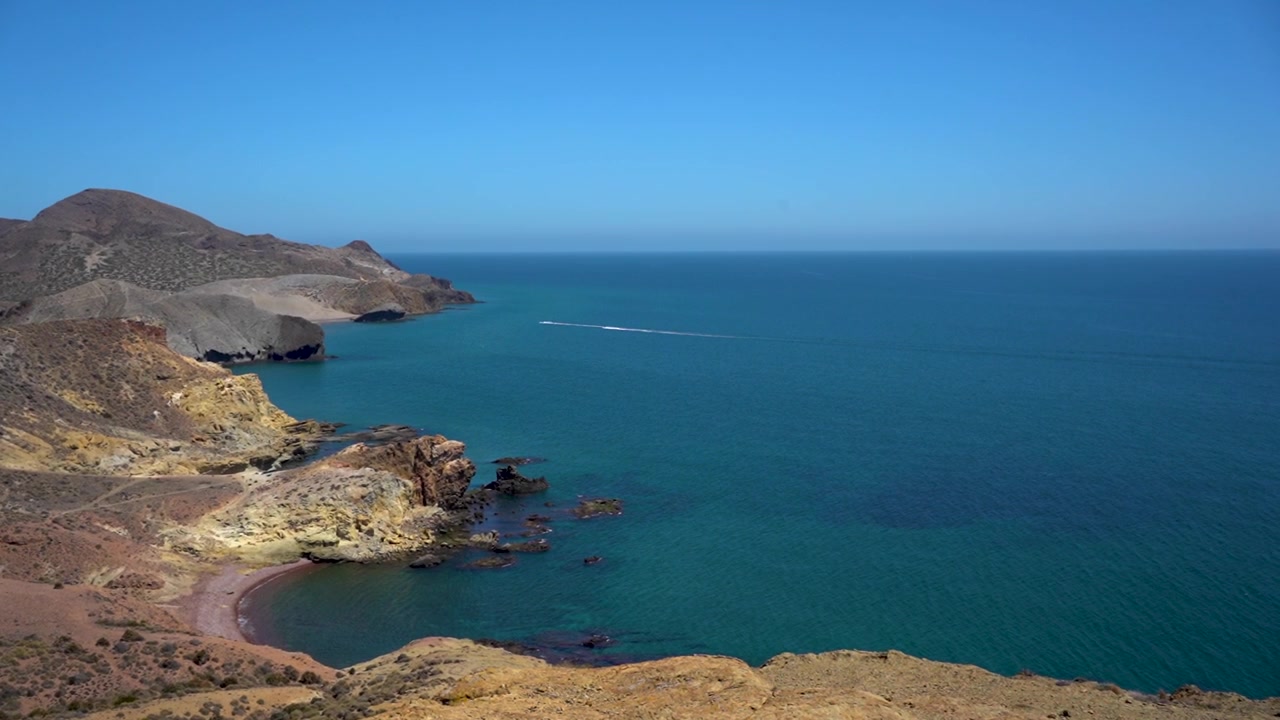 Scogliere costiere mozzafiato che incontrano il mare azzurro brillante sotto un sole splendente, vista aerea
