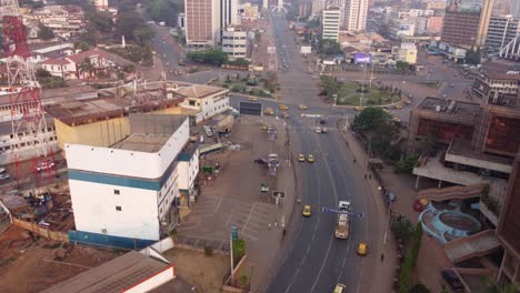 Tráfico-En-El-Centro-De-Yaundé-Con-Muchos-Taxis-Amarillos-Dando-Vueltas-En-La-Rotonda,-Plataforma-Rodante-Aérea-A-La-Vista